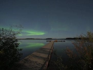 A wooden pier stretches into a calm lake under the northern lights.
