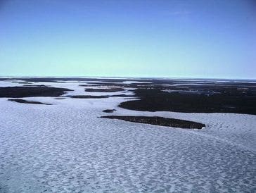 Frozen landscape with patches of snow and water under a clear sky.