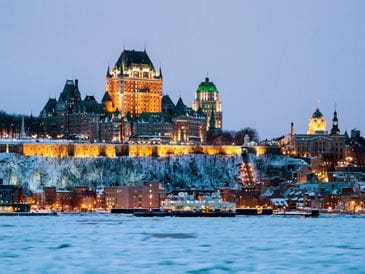 City skyline at dusk with illuminated historic buildings by the water.