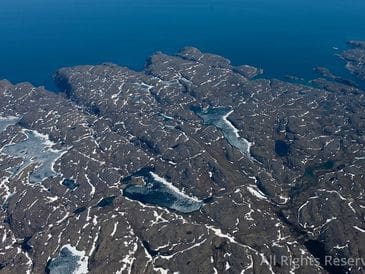 Aerial view of rugged, snow-dotted rocky islands in blue water.