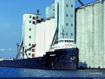 A large cargo ship docked near tall grain silos at a port.