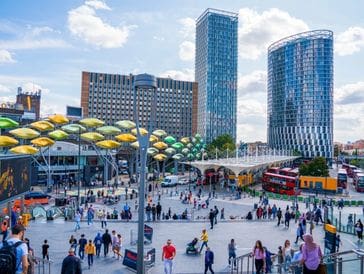 A busy urban plaza with colorful umbrellas and modern skyscrapers.