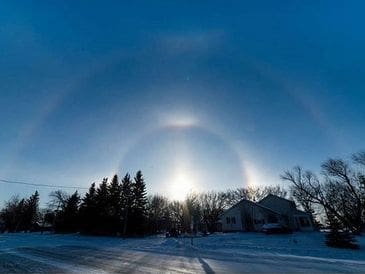Sun halo glowing above snowy houses and trees at dusk.