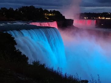 Niagara Falls illuminated with vibrant blue and pink lights at night.