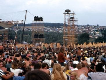 Large outdoor concert with a crowd and stage setup in a hilly area.