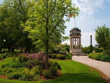 A peaceful garden with a monument and lush greenery under a partly cloudy sky.