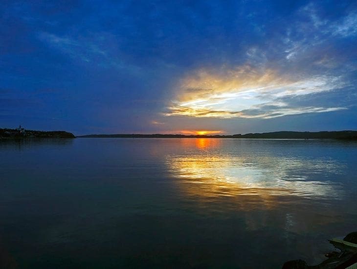 Sunset over calm lake waters with vibrant sky reflections.