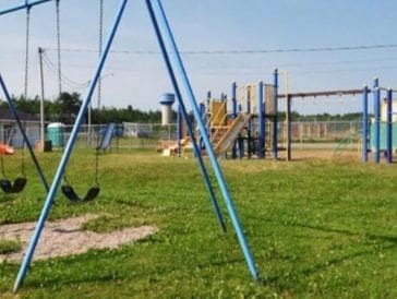 Empty playground with swings and climbing structures on a sunny day.