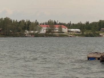 A large house with a red roof by the water surrounded by trees.