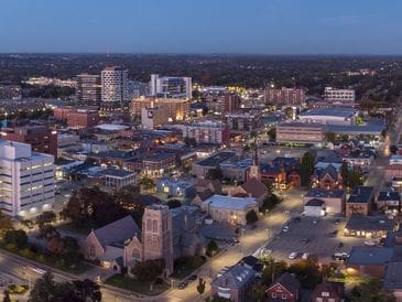 A cityscape at dusk with buildings and streetlights illuminating the scene.