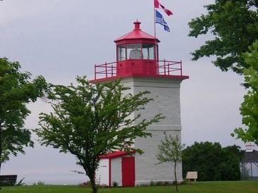 A red and white lighthouse standing near a tree under a cloudy sky.