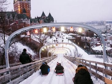 People sledding down snowy hills with cityscape in background.
