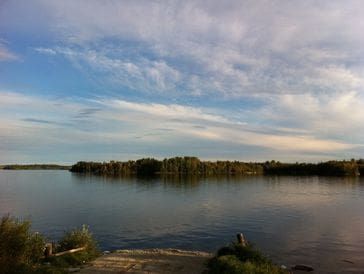 A calm lake under a sky with scattered clouds at sunset.