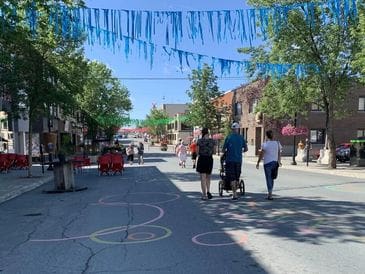 People walk down a decorated street on a sunny day.