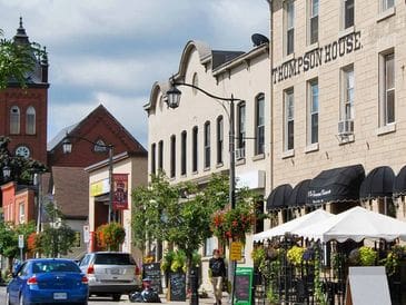 A lively street with shops, outdoor seating, and pedestrians on a sunny day.