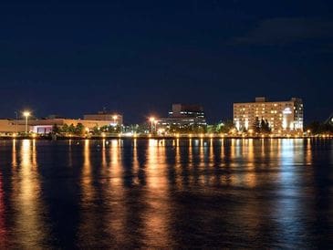 Nighttime cityscape with illuminated buildings reflecting on calm water.