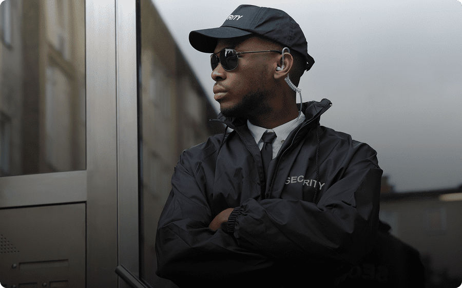 Man in sunglasses and cap leaning against a reflective surface with arms crossed.