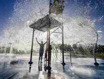 Person standing under a splash of water at a playground.