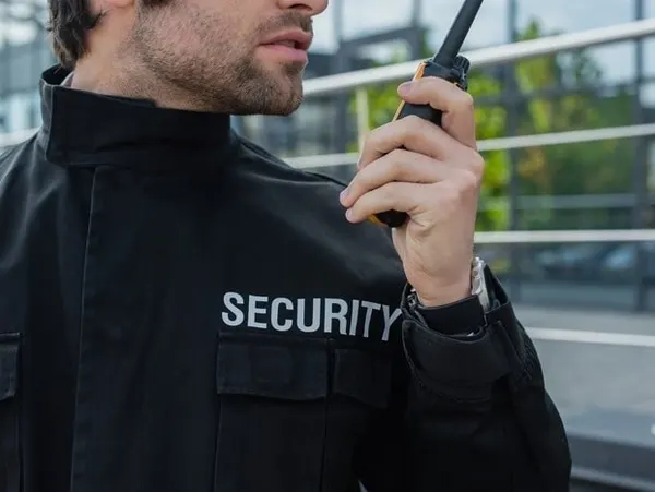 Security guard speaking into a walkie-talkie outdoors.