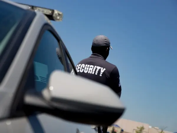 Security guard standing near a vehicle under a clear blue sky.