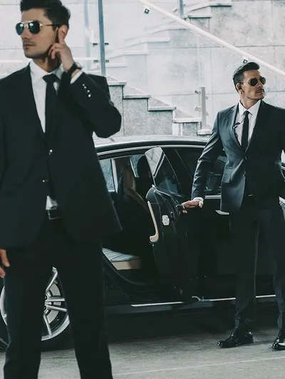 Two men in suits near a luxury car, one talking on phone.