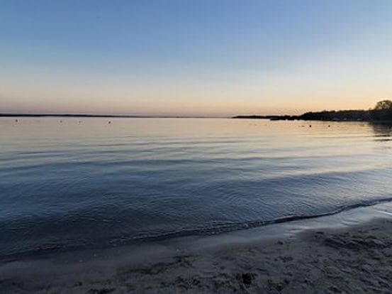 Calm sea at sunset with a clear sky and sandy shore.