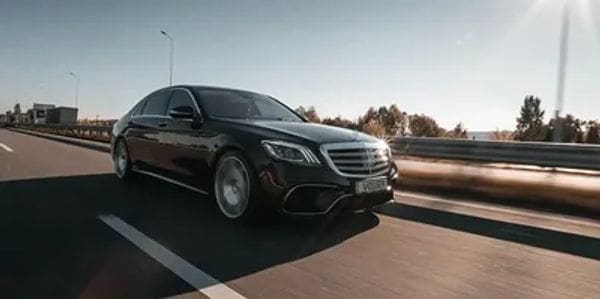 A sleek black Mercedes-Benz driving on a highway at sunset.