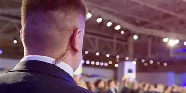 Man in an earpiece at a conference or event, facing an audience.