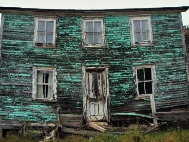 Old, weathered green wooden house with peeling paint and broken windows.