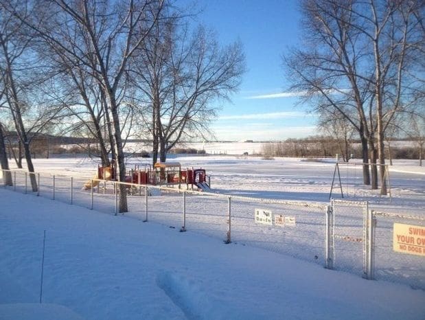 Snow-covered playground with swings and a clear blue sky.