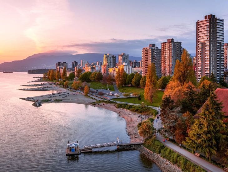 Sunset over a city waterfront with autumn trees and mountains.