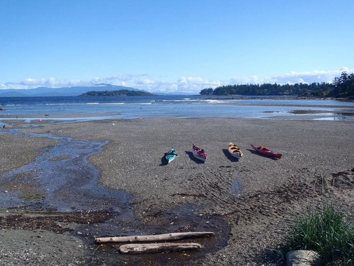 Colorful kayaks resting on a serene beach with islands in the distance.