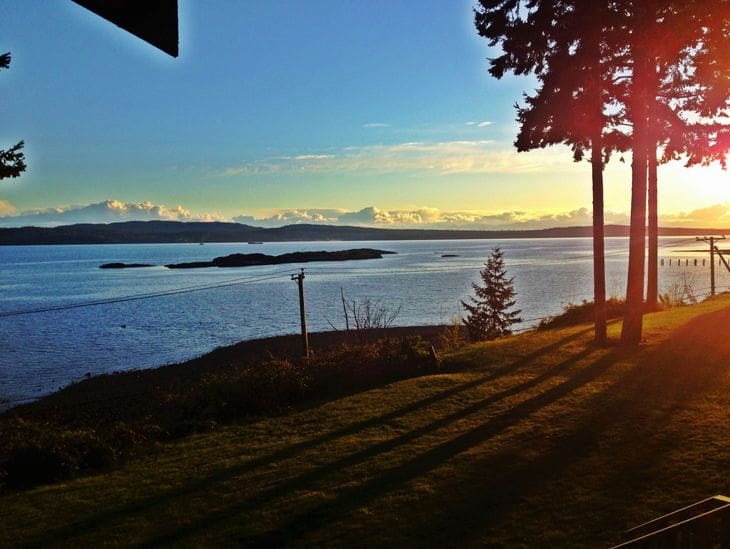 Sunset casting long shadows over a calm lakeside with distant mountains.