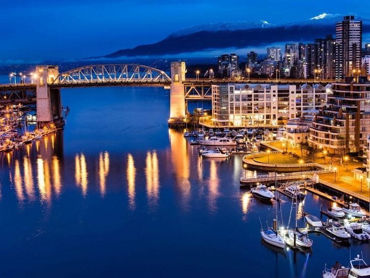 Night view of a lit-up bridge and marina reflecting on calm water.