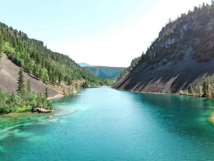 Tranquil turquoise lake nestled between forested hills under a clear sky.