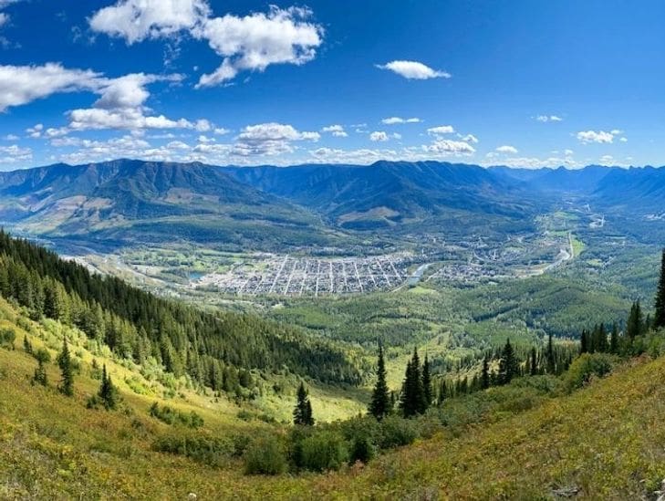 Scenic mountain valley with a town nestled below under a bright blue sky.