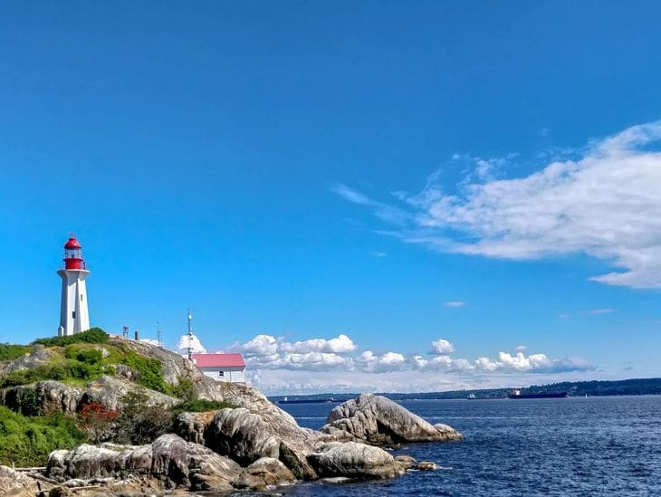 Scenic coastal view with a lighthouse and rocky shore under a bright blue sky.