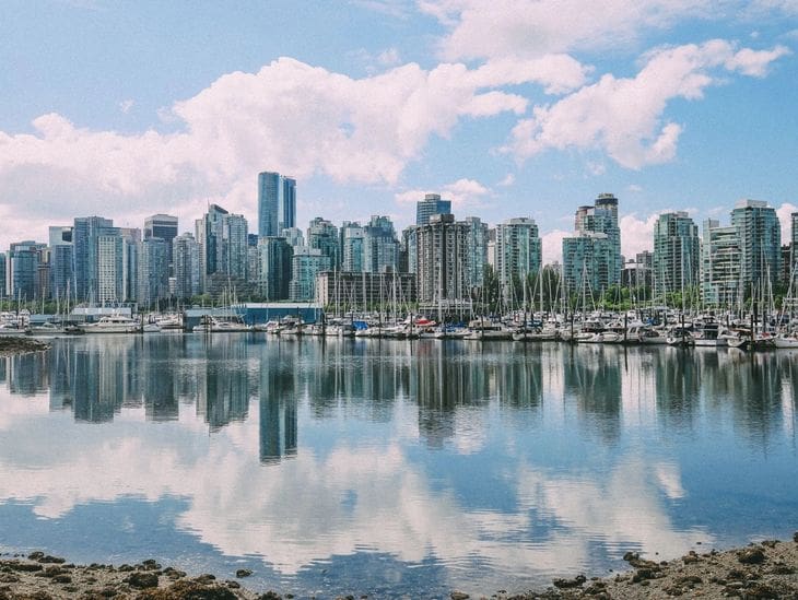City skyline reflected on calm water under a partly cloudy sky.