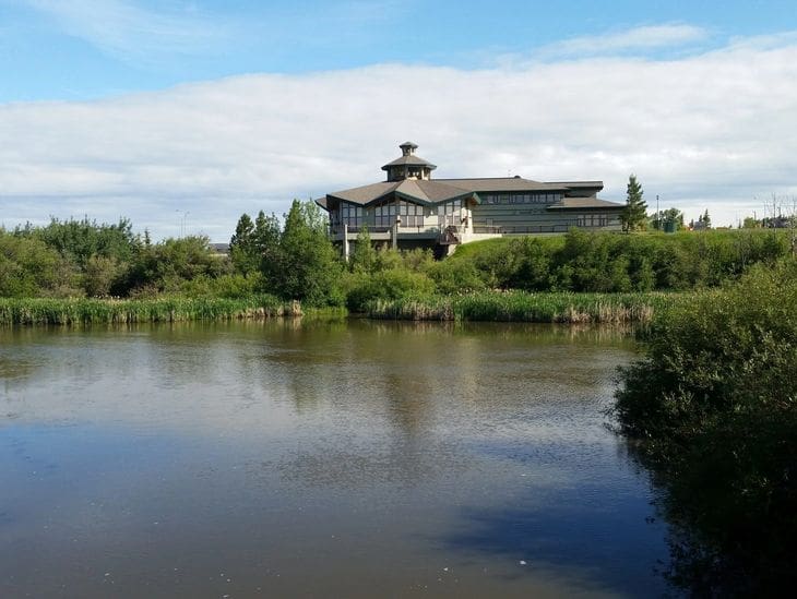 A large building with traditional architecture by a calm lake under a partly cloudy sky.
