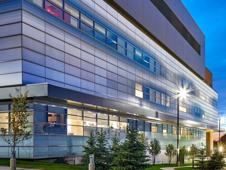 Modern building exterior illuminated at dusk with greenery in front.