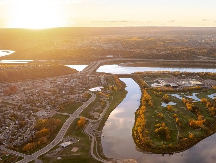 Aerial view of a winding river at sunset with surrounding roads and greenery.