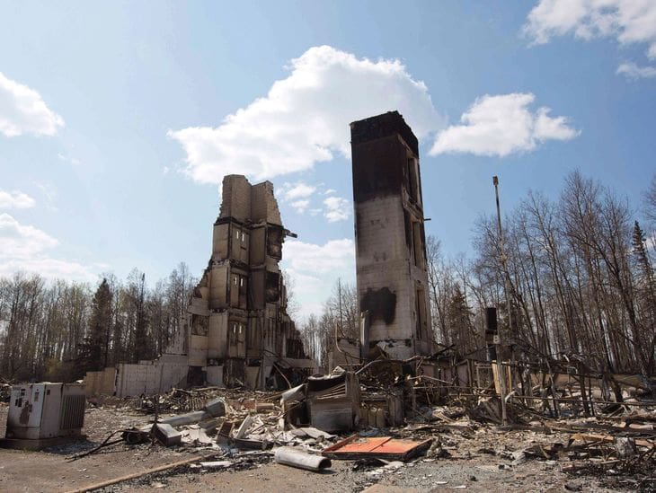 Destroyed buildings stand amidst rubble under a partly cloudy sky.