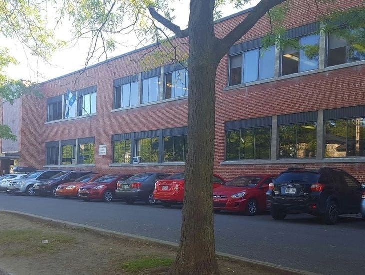 Brick office building with parked cars and a tree in front.