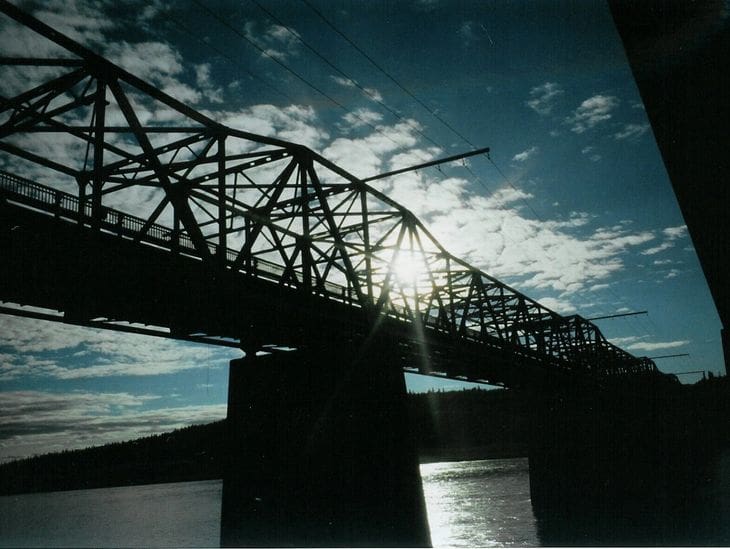 Silhouette of a bridge against a setting sun under a cloudy sky.