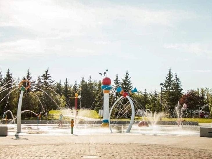 Colorful fountain sculpture with water jets in a park setting.