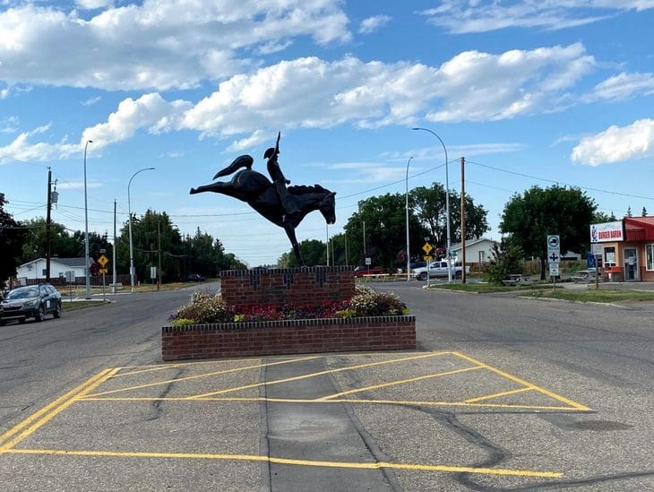 Bronze statue of a cyclist on a horse in an urban setting under a blue sky.