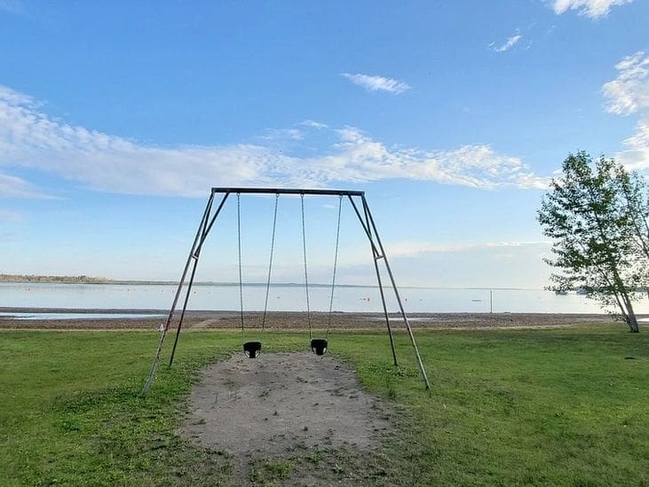 Empty swingset by a calm lakeside under a blue sky.