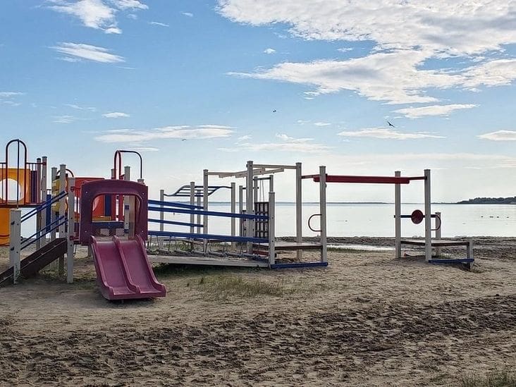 A deserted playground with a slide and climbing structure on a sandy beach.